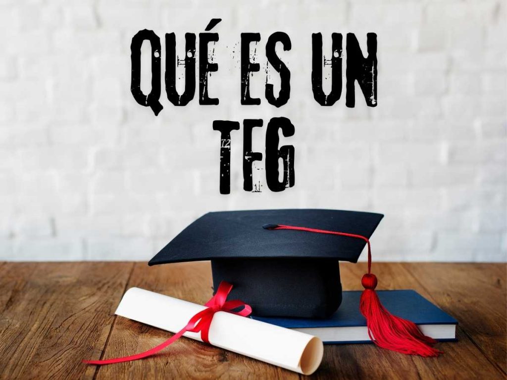 Birrete de graduación y diploma sobre una mesa con el texto 'Qué es un TFG' en la pared