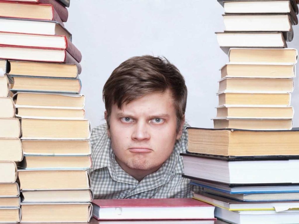 Joven rodeado de pilas de libros mirando hacia la cámara