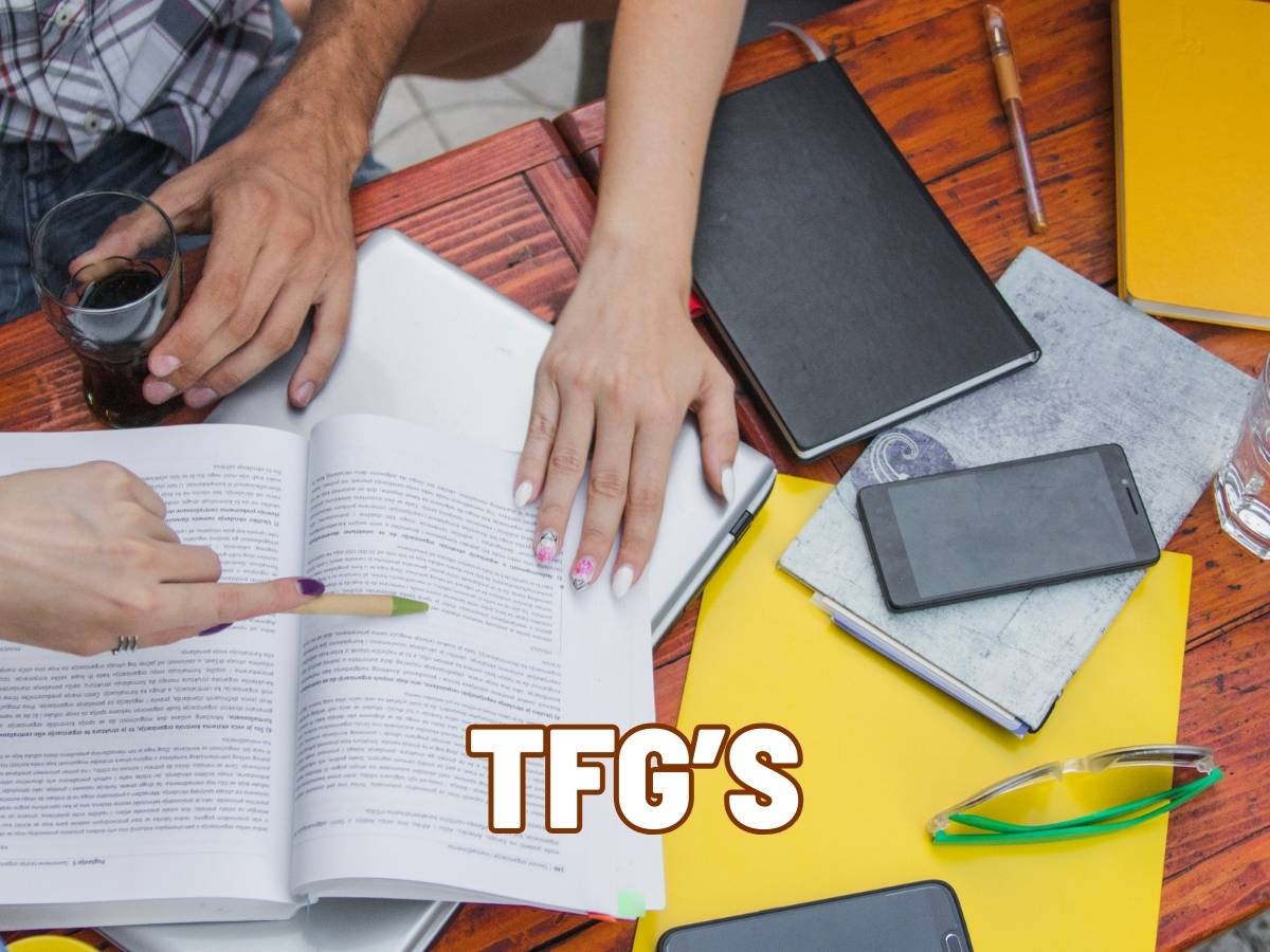 Manos de estudiantes revisando notas y material de estudio para un TFG en una mesa.