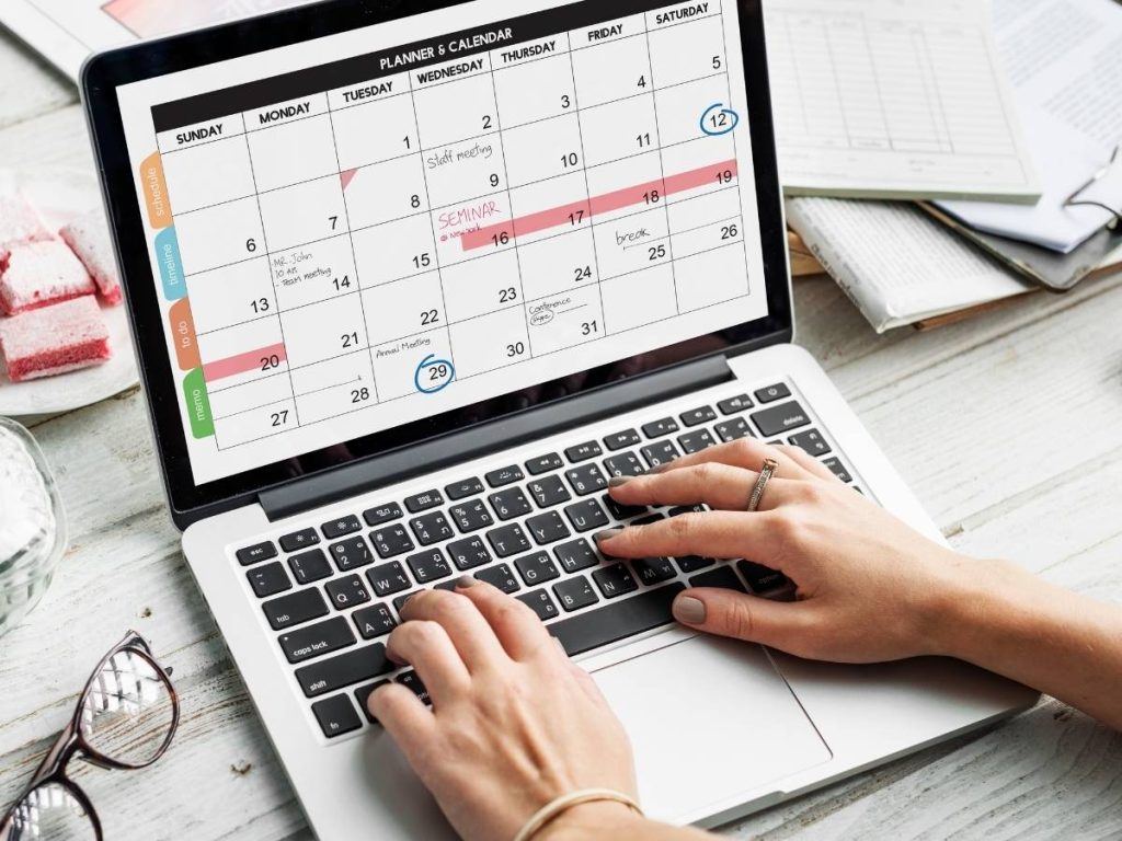 Persona usando una laptop para crear un cronograma detallado para su Trabajo de Fin de Grado, mostrando un calendario en la pantalla.