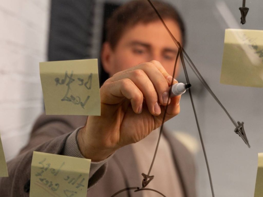 Estudiante masculino trazando un diagrama en una pizarra, ilustrando el proceso de organización y desarrollo de un TFG.