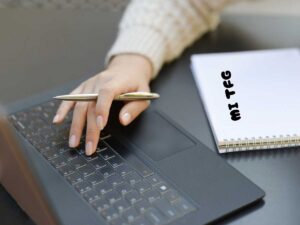 Persona investigando y escribiendo su Trabajo de Fin de Grado con un cuaderno al lado del teclado.