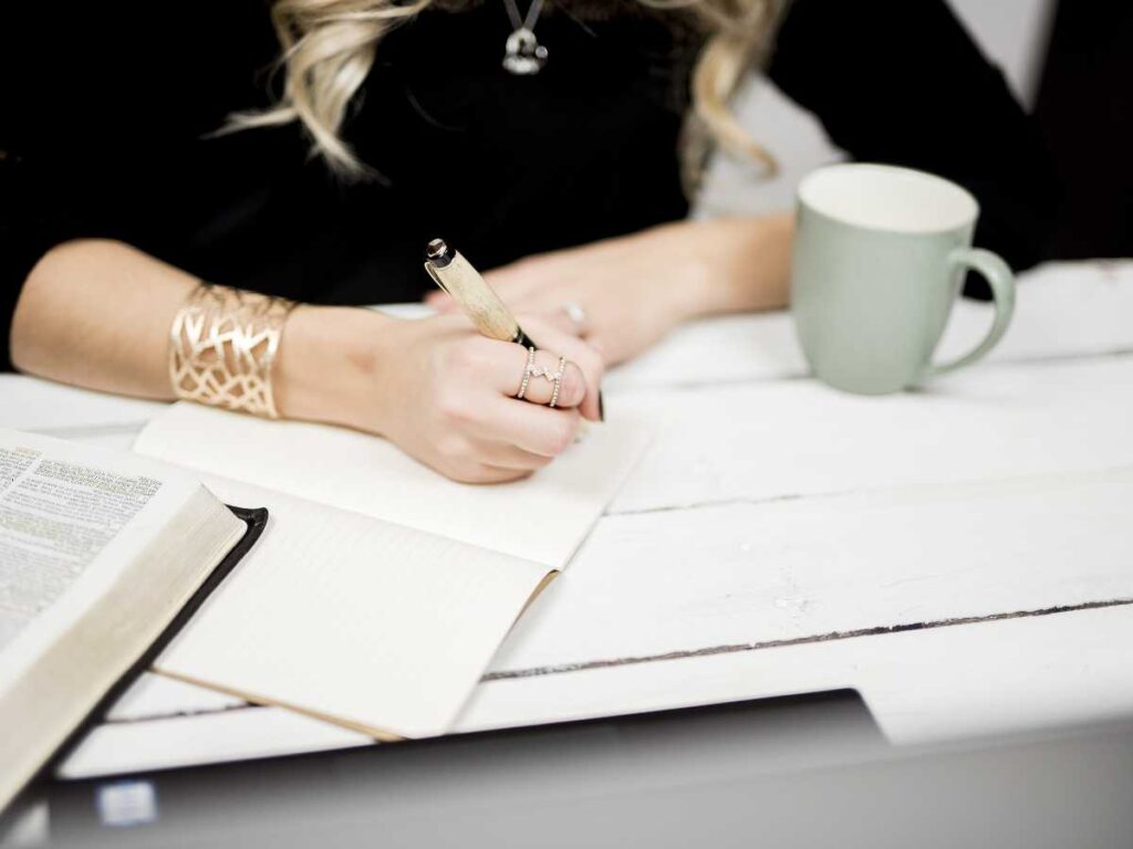 Mano escribiendo en una mesa con documentos y una taza mientras formula una hipótesis para el TFG.