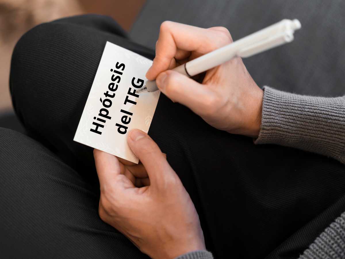 Persona escribiendo sobre una hoja la hipótesis de su TFG.