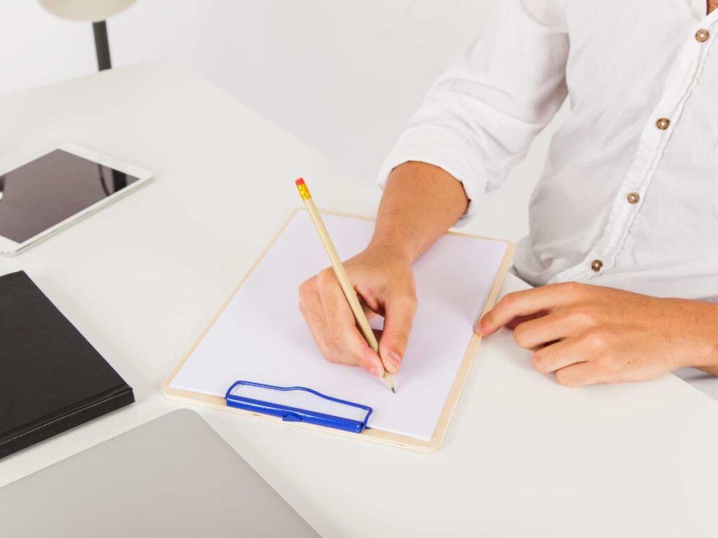 Persona escribiendo un trabajo académico en un escritorio blanco