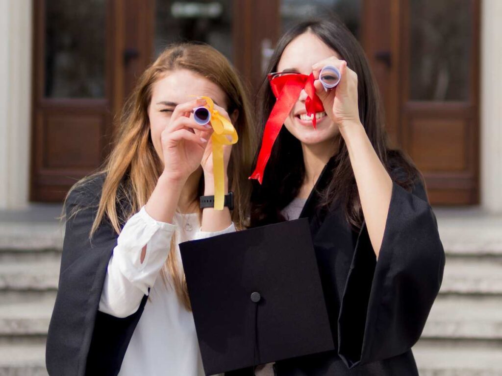 Dos estudiantes celebrando la graduación con birrete y diploma