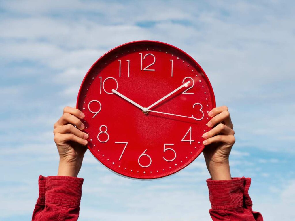 Persona sujetando un reloj rojo frente a su cara sobre fondo azul